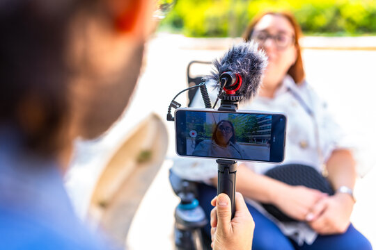 Videographer recording interview with businesswoman in wheelchair outdoors
