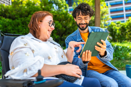 Smiling friends using tablet in a park, woman sitting in a wheelchair