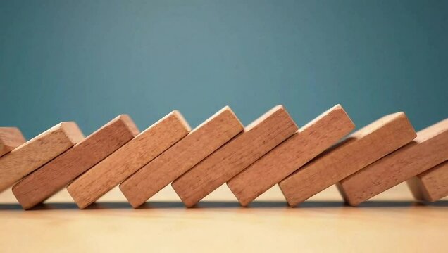 Side view of a row of wooden dominoes toppling over in quick succession on a tabletop.
