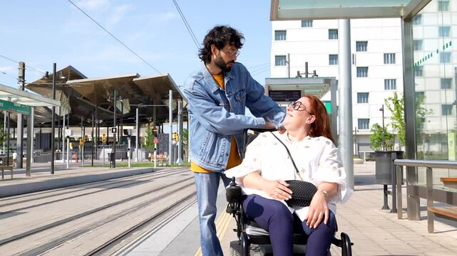 Caring boyfriend providing supportive assistance to girlfriend using wheelchair at urban transportation platform, showcasing deep emotional connection and inclusivity