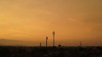 Silhouetted Communication Towers Against a Warm, Golden Sunset Sky Over City