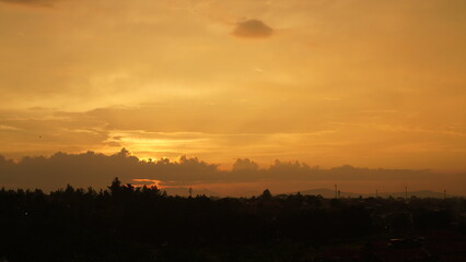 Golden Hour Over Silhouette Trees and Distant Cityscape Under Cloudy Sky