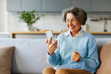 Happy elderly woman using smartphone at home, making video call, consulting doctor at virtual meeting on mobile phone and smiling at screen