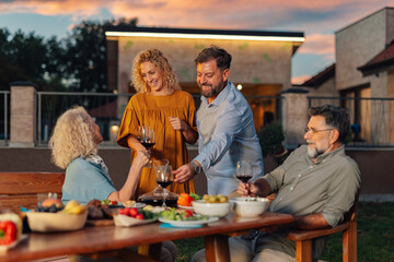 Family enjoying dinner together in the backyard at sunset, pouring wine and eating healthy food