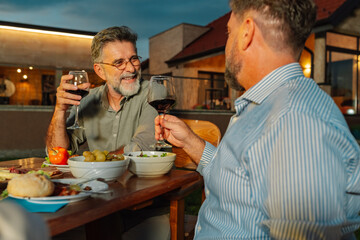 Two senior men enjoying wine and food at a backyard dinner party