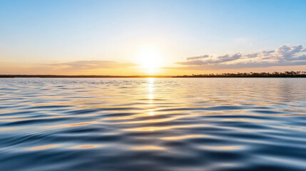 Obraz premium Serene water surface reflecting sunset sky with gentle waves and soft clouds