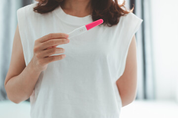 Close-up of a young woman holding a pregnancy test in her hands. She checks the pregnancy exam and discovers her positive pregnancy test. People, Healthcare, Medical and Family planning concept.