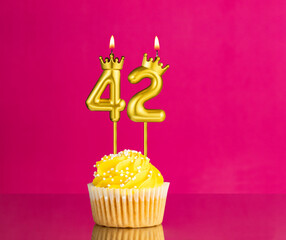Yellow birthday cupcake with a number 42 candle - Birthday card on a pink background
