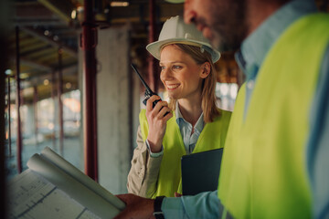 Female architect using walkie talkie while discussing blueprint with foreman at construction site