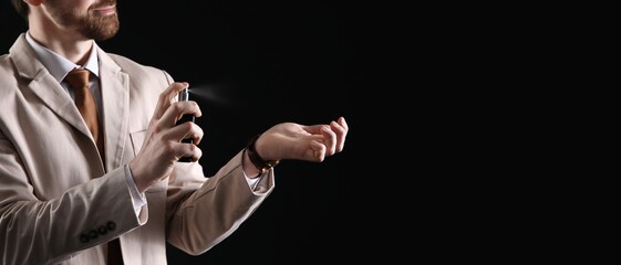 Handsome man in light suit applying perfume against black background with space for text