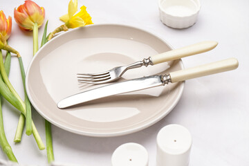 Composition with clean plate, crockery and beautiful flowers on white background