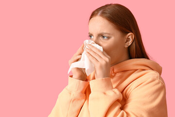 Allergic young woman sneezing into tissue on pink background