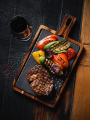 Grilled ribeye steak served on a dark slate plate with vegetables