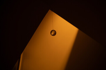 Chrystal glass ball hanging and reflecting light in a white wall staircase under dim light.