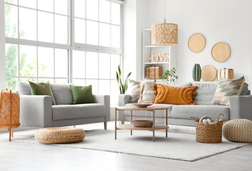 Interior of light living room with grey sofas, coffee table and wicker poufs