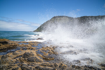 Large Waves Splash on Rocky Shore Under Blue Sky