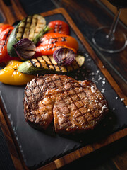 Grilled ribeye steak served on a dark slate plate with vegetables