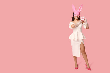Beautiful young happy Asian woman in bunny mask with gift box on pink background