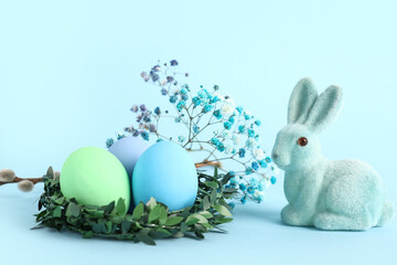 Green nest with painted Easter eggs, gypsophila flowers and bunny on blue background