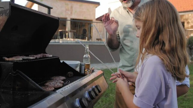 Children learning grilling techniques from adults in backyard