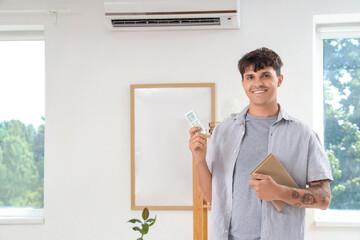 Fototapeta premium Young man with book turning on air conditioner at home