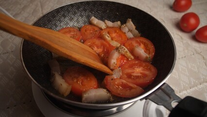 Fresh tomatoes and tender pork are being sauteed in a skillet, highlighting the culinary process in a cozy kitchen setting during evening hours.