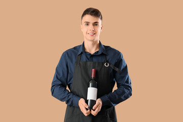 Naklejka premium Young male waiter with bottle of wine on beige background
