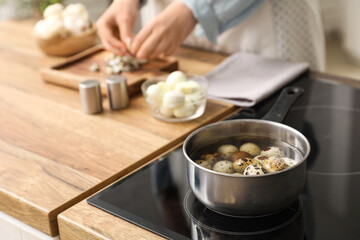 Woman peeling quail eggs in kitchen, focus on cooking pot with boiling eggs