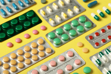 Different pills in blister packs on yellow background, closeup