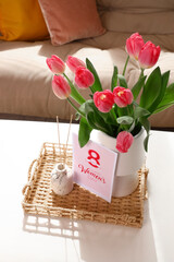 Vase with tulips, reed diffuser and greeting card for Women's Day on table in living room