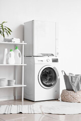 Interior of laundry room with modern washing machine and clothes dryer near white wall
