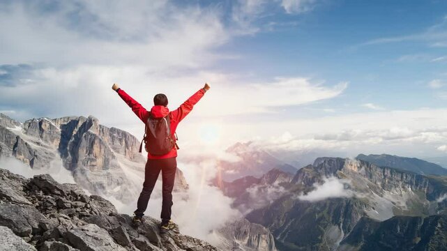 A triumphant hiker raises both arms atop a rocky peak above swirling clouds. Concept of adventure success and personal achievement.