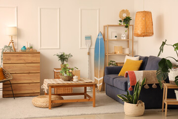 Interior of stylish living room with grey sofa, coffee table, houseplants and surfboard
