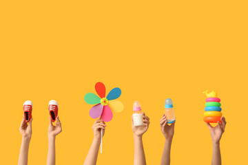 Hands holding baby accessories on yellow background