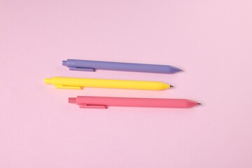 Set of ballpoint pens on pink background, flat lay