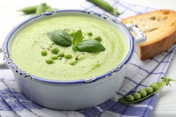 Tasty pea cream soup with basil served on white wooden table, closeup