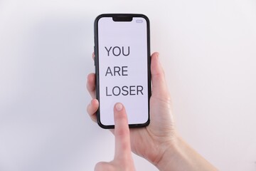Cyber bullying. Woman holding smartphone with text You Are Loser on white background, closeup