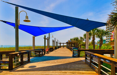 A view down a wooden beach boardwalk with shade tarps and their shadows at Carolina Beach, North Carolina USA.