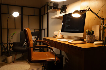 Interior of dark office with programmer's workplace, armchair and glowing lamps