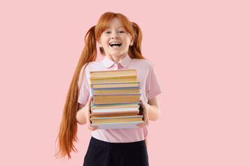 Cute redhead schoolgirl with stack of books on pink background