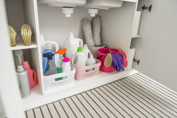 Open drawer with baskets of different cleaning supplies, brushes, rubber gloves and pp-dusters in...