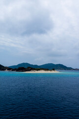 Aka Island’s serene coast, seen from Zamami Ferry— turquoise waters, and lush hills.
