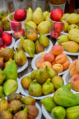 Colorful display of fresh fruits, including ripe figs, pears, apricots, and red apples, arranged on plates and in cups at local market. Essence of seasonal abundance and healthy eating