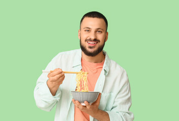 Young man eating tasty ramen on green background