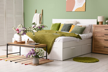 Interior of stylish spring bedroom with bed, ladder, commode and beautiful flowers bouquets in...