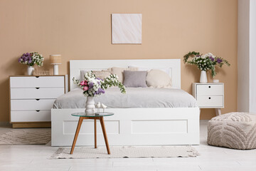 Interior of stylish spring bedroom with bed, commode and beautiful flowers bouquets in vases on...