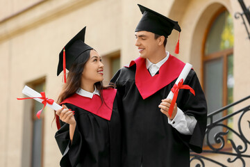 Couple of happy graduating students with diplomas hugging near university