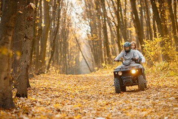 Man and woman driving quad bike in autumn forest