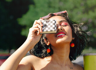 A girl with pink makeup and glasses takes a photo with a retro checkerboard camera