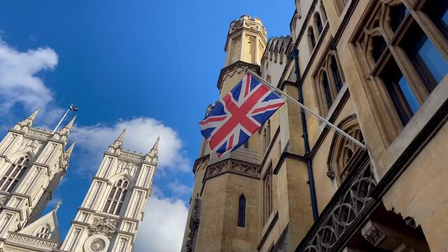 Union Jack British flag waving proudly beside the grand towers of Westminster Abbey beneath a brilliant blue English sky
